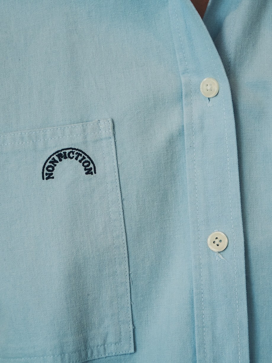 Close-up of pale blue chambray shirt with subtle Nonfiction brand logo embroidered on chest pocket