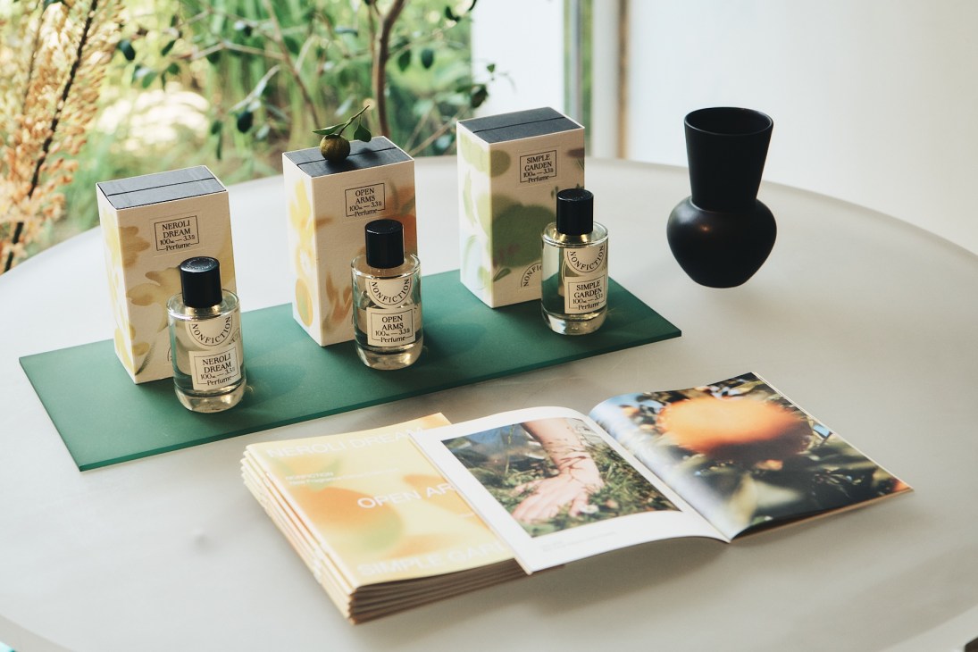 Three small perfume bottles and packaging boxes arranged on a green surface with an open magazine