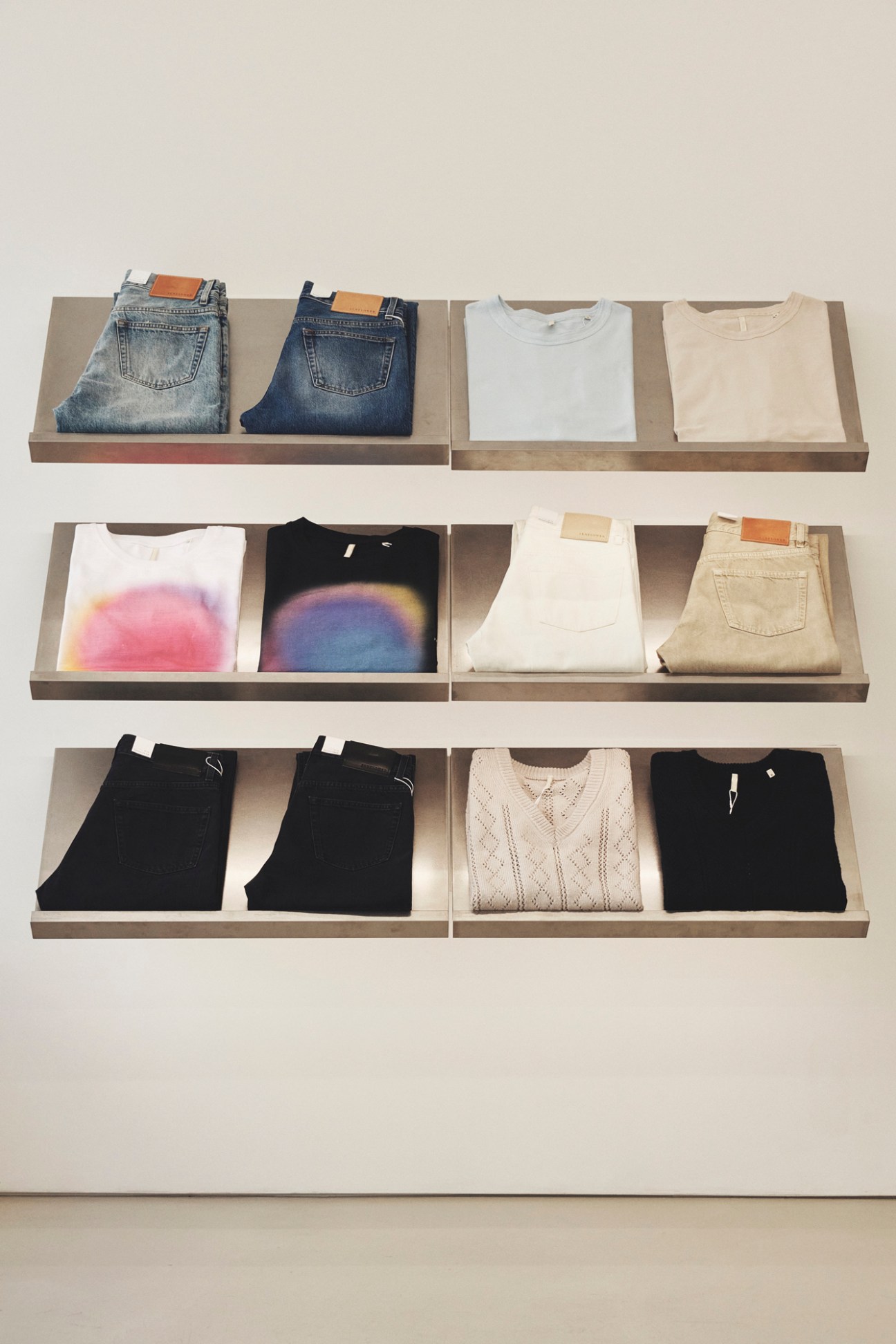 Neatly folded clothing displayed on wooden shelves including jeans, t-shirts, and knitwear