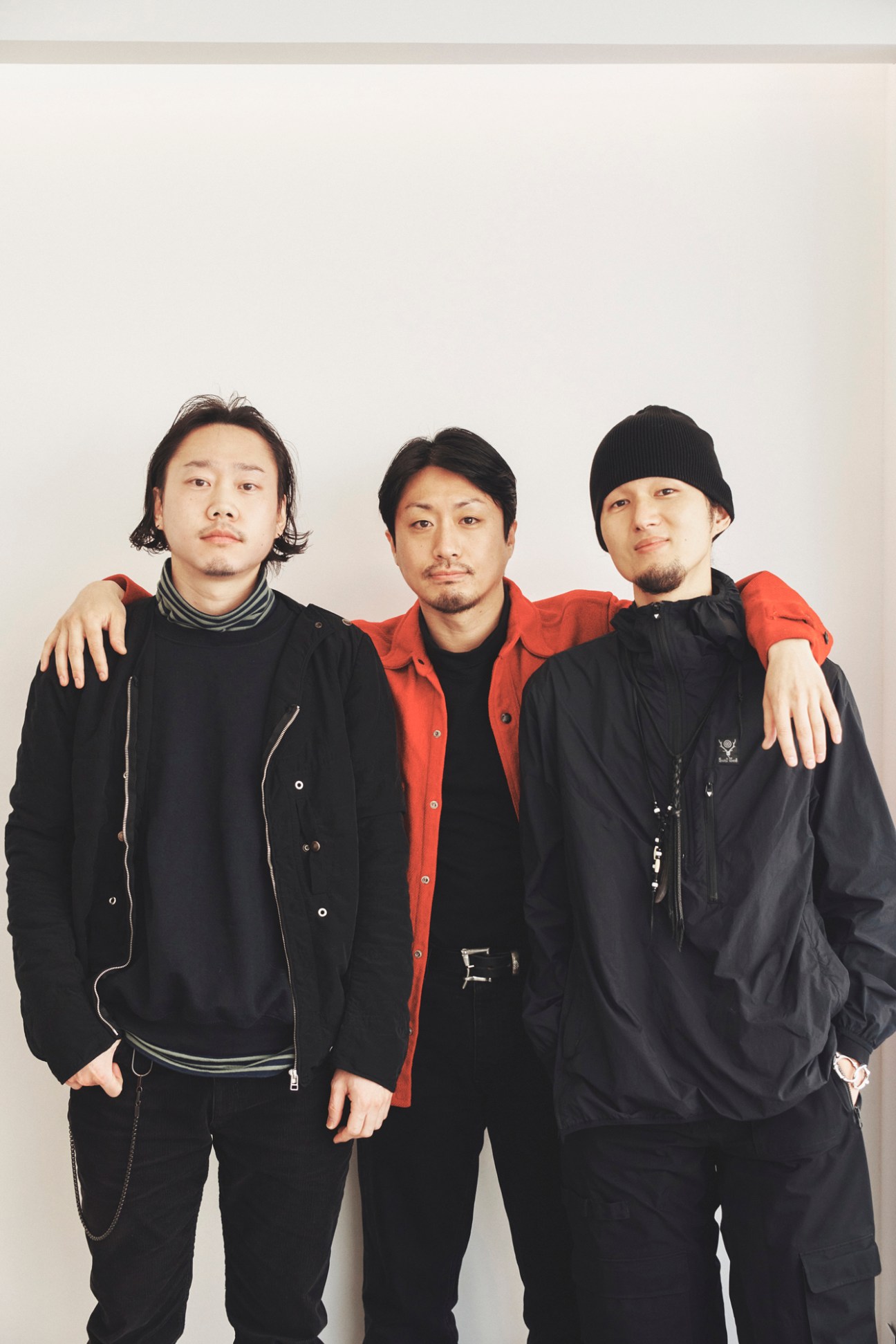 Three men posing together, wearing black and red casual menswear