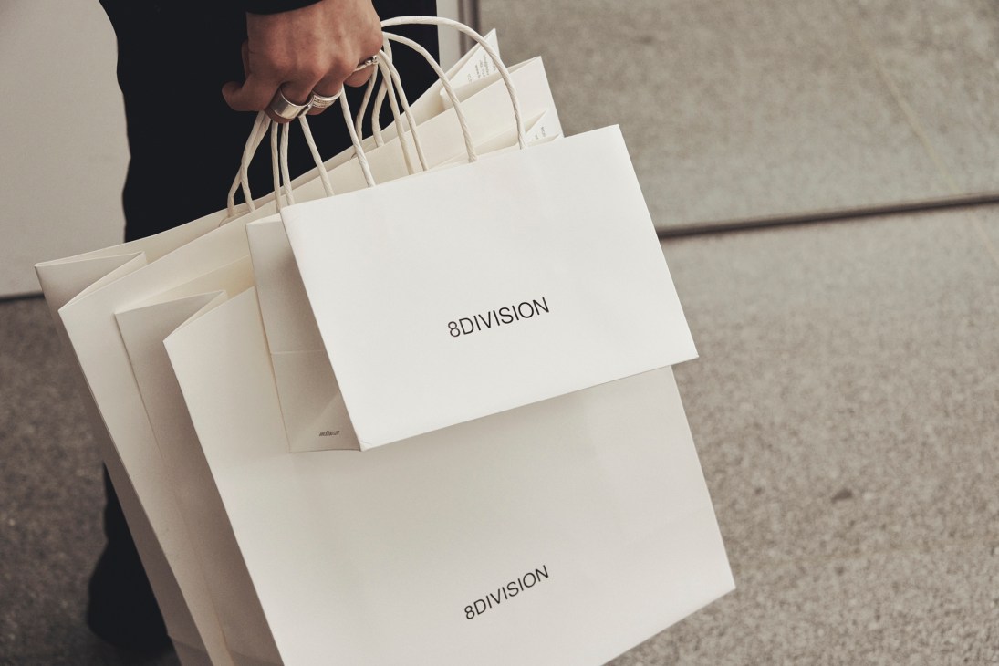 Person carrying multiple white 8Division shopping bags on concrete steps