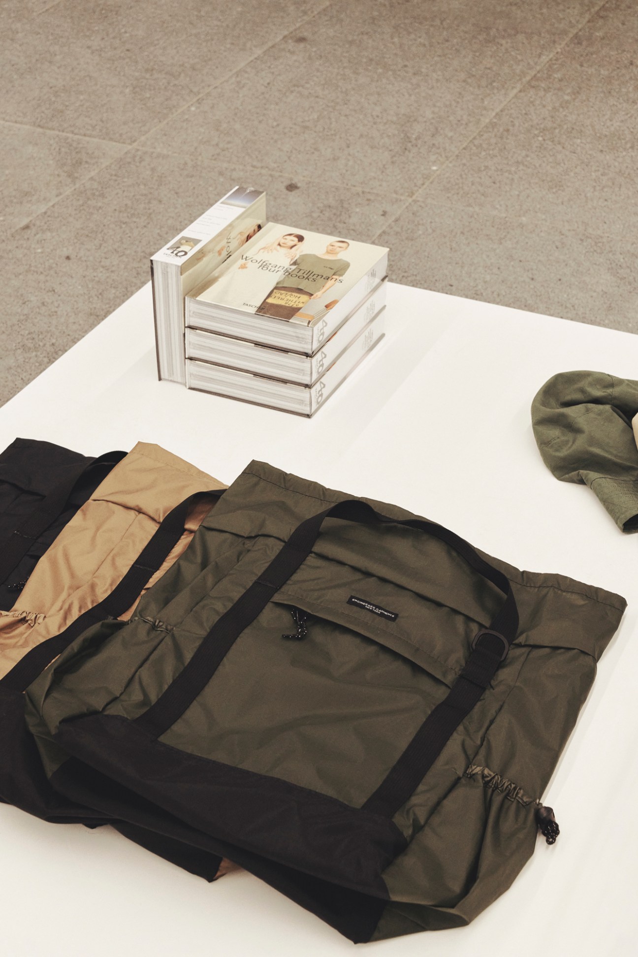 8Division menswear store interior with olive duffel bag, books and cap on white display table