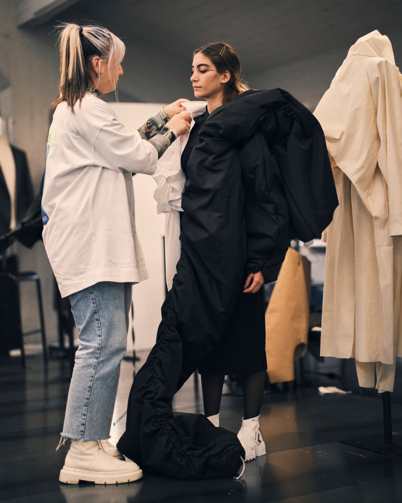 Two students in a fashion classroom, one fitting a black garment on another who is wearing protective covering