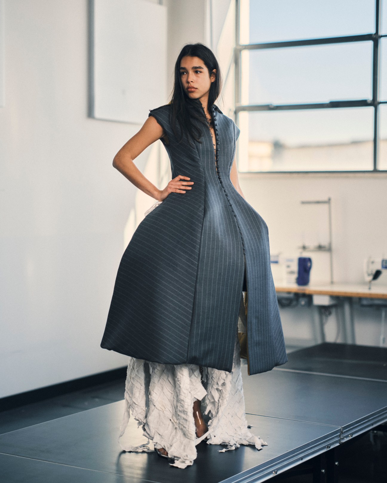 Woman in dark pinstriped dress over white layered skirt in modern studio space