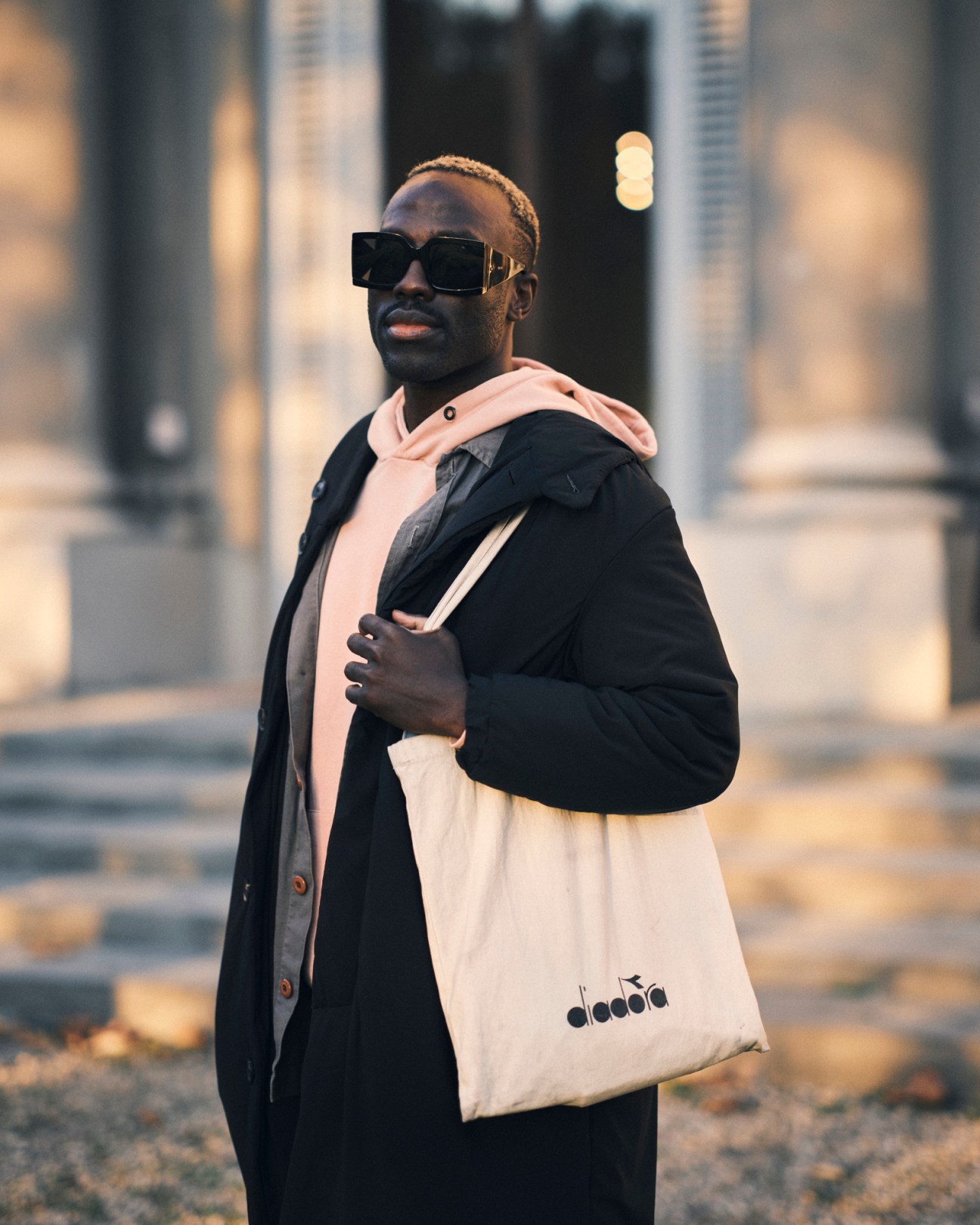 Cecil Kadenyi wearing sunglasses and layered clothing while carrying a canvas tote bag