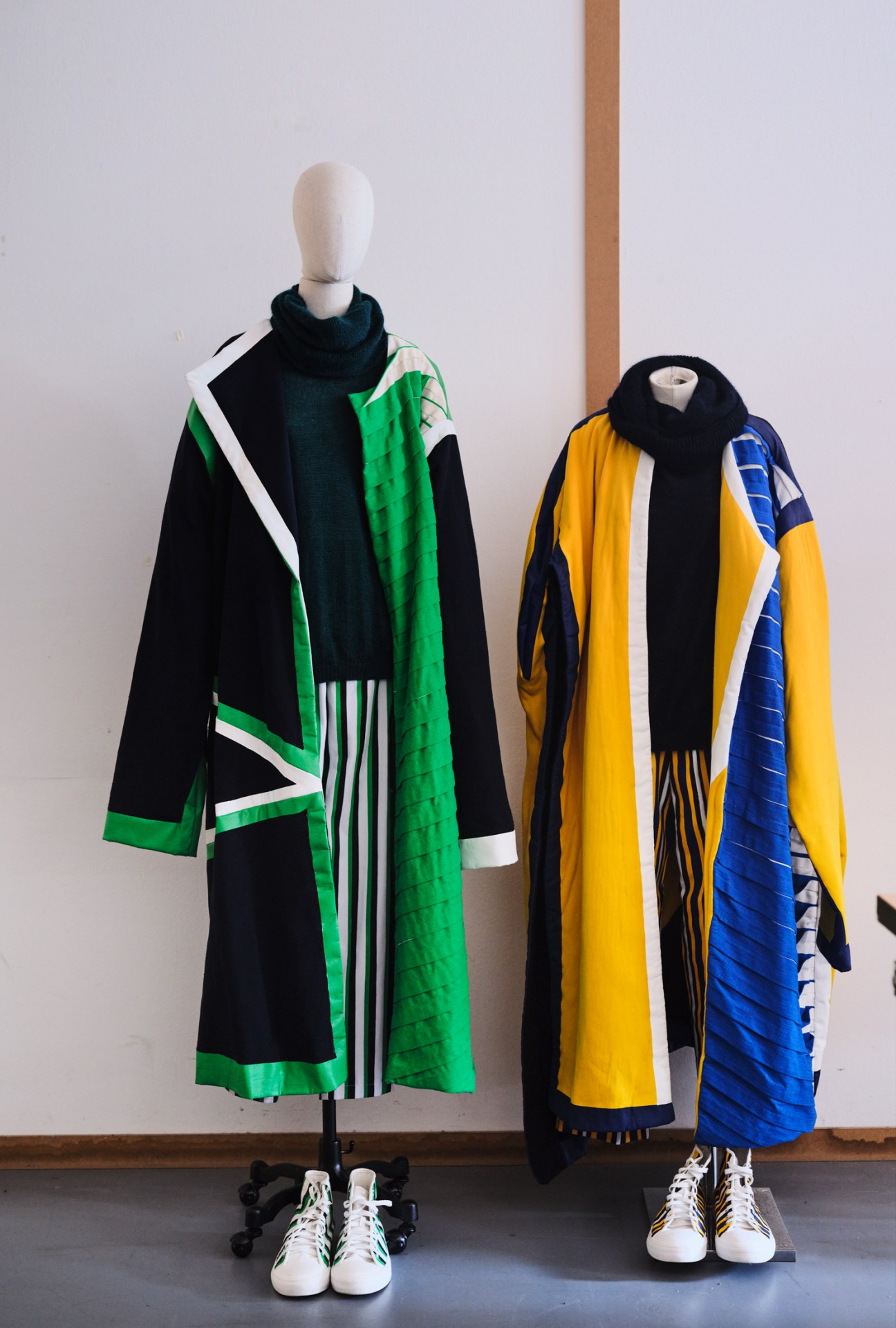Two mannequins displaying colorful student fashion designs with geometric patterns and draped fabrics