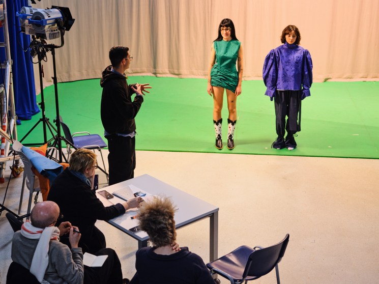 Behind-the-scenes photo shoot with two models in green and purple outfits against green screen backdrop
