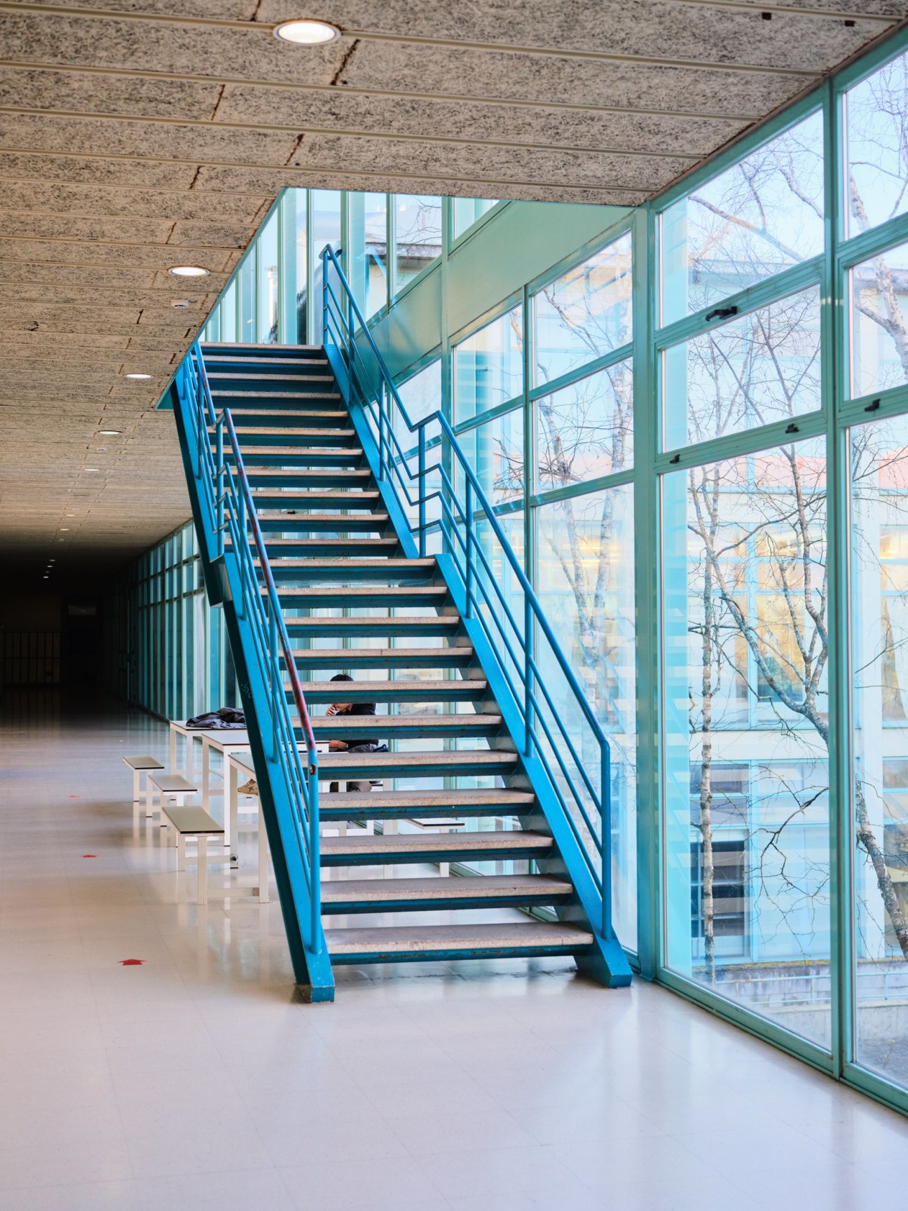 Modern interior with blue metal staircase and floor-to-ceiling windows overlooking bare trees