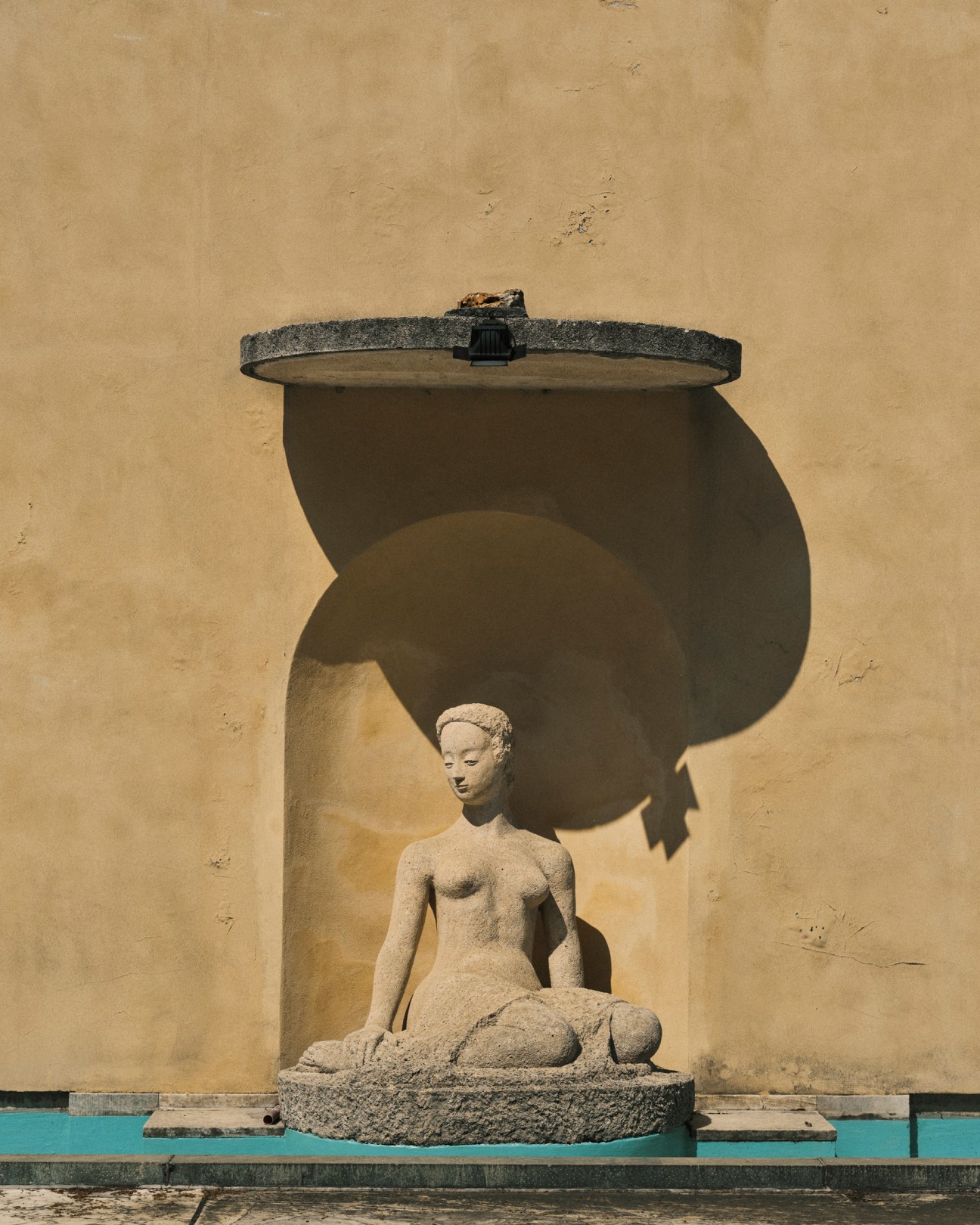 Stone sculpture of seated female figure in classical style positioned under curved architectural canopy