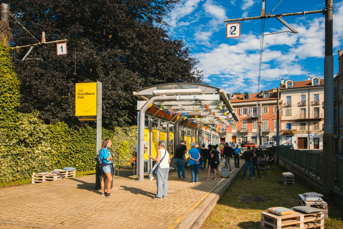 People gathered at covered tram station platform with colorful bunting and wooden seating areas in Turin