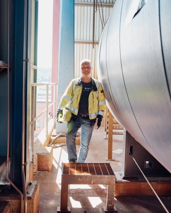 Plant manager in high-visibility jacket standing between large industrial pipes at Sekab Biorefinery.