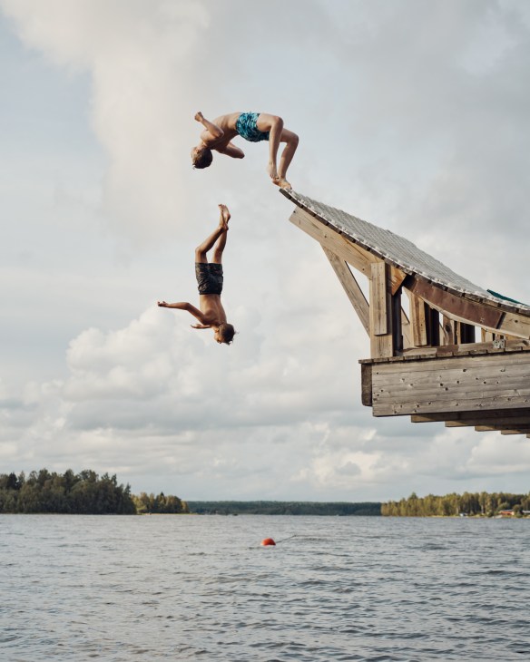 Two children backflip off a wooden ski jump platform into water in Obbola, Sweden.