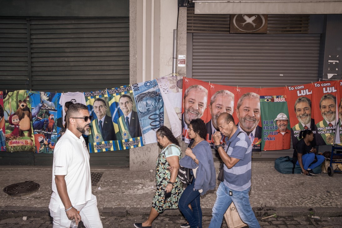 Street vendor displaying towels featuring portraits of presidential candidates Lula and Bolsonaro hanging on a line