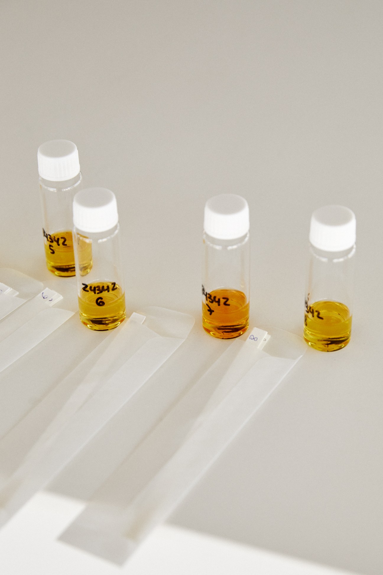 Four small glass vials with white caps containing yellow fragrance ingredients arranged on a white surface