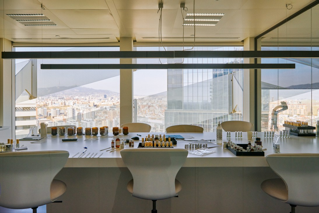 Modern perfumery lab with white tables, bottles, testing equipment and city views through floor-to-ceiling windows