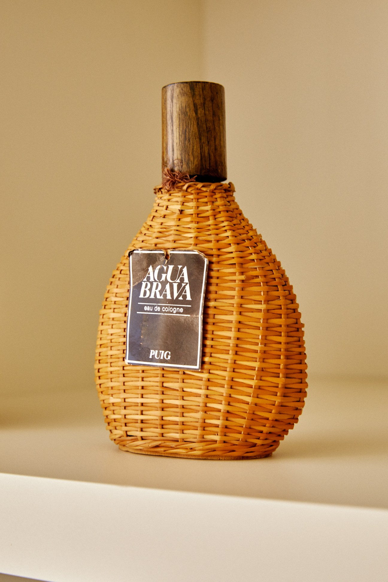 A woven wicker perfume bottle with wooden cap and Agua Brava label by Puig