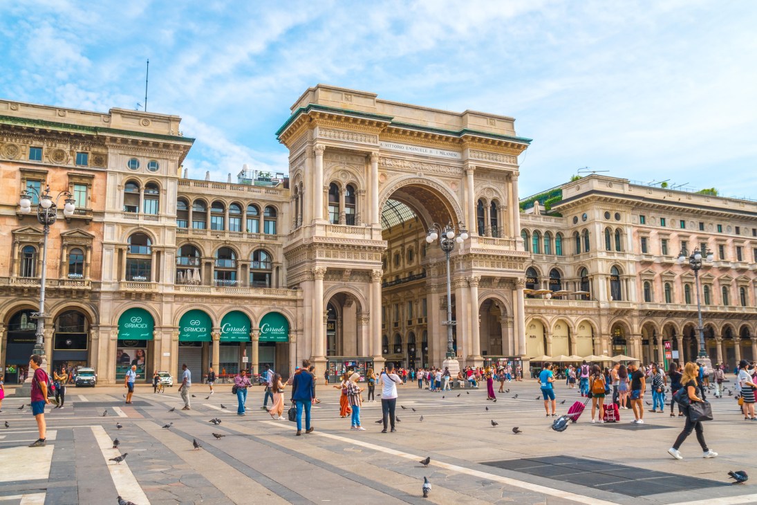 Historic Milan piazza with ornate architecture and people walking across the square