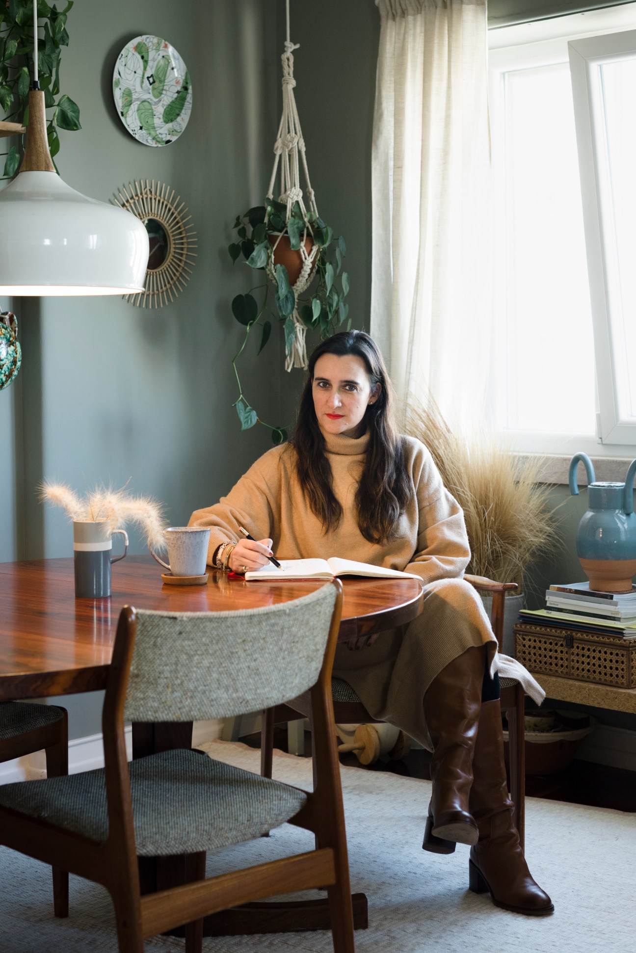 Joana Astolfi, founder of Studio Astolfi window display company, sitting at wooden table writing in notebook