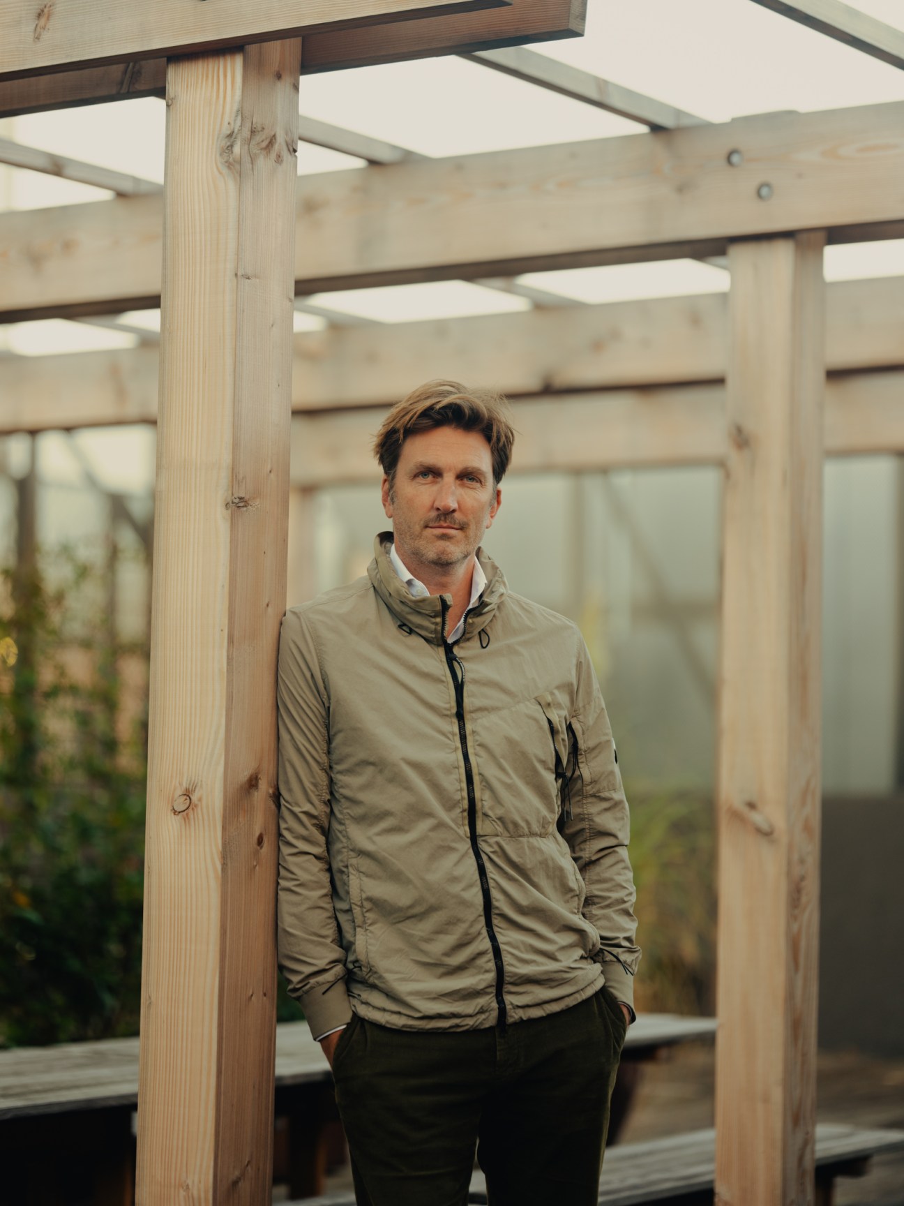 Claus Mathisen, CEO of NREP, stands in a greenhouse structure wearing a beige jacket.