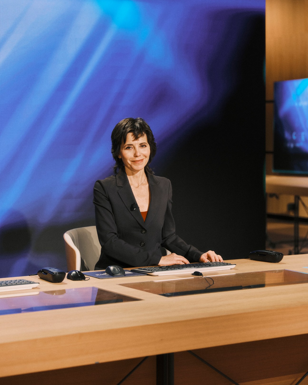 Journalist Emanuela Bonchino sitting at a wooden desk in the Renzo Piano-designed Rai News 24 television studio
