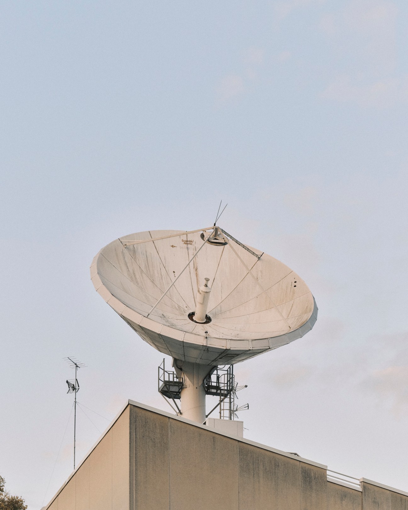 Large white parabolic satellite dish antenna mounted on top of concrete building against pale sky