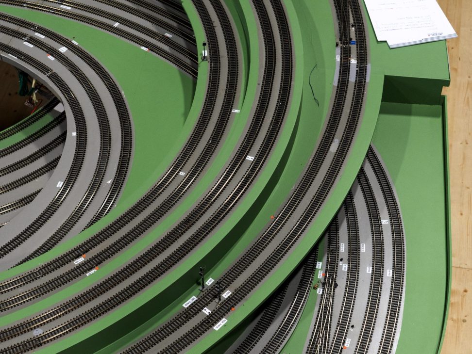 Curved model railway tracks with multiple parallel lines on green baseboard in laboratory setting