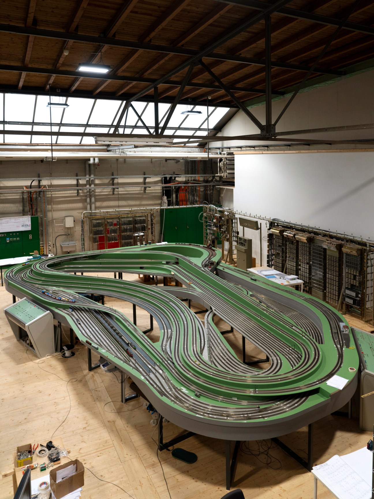 Large model railway setup with multiple curved tracks and green surface in industrial warehouse space