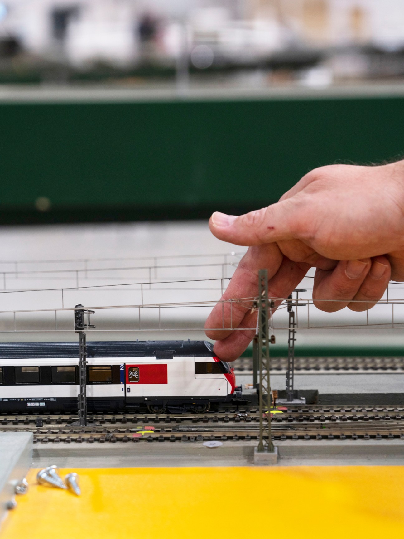 Hand reaching toward model railway train with overhead power lines and miniature landscape in laboratory setting