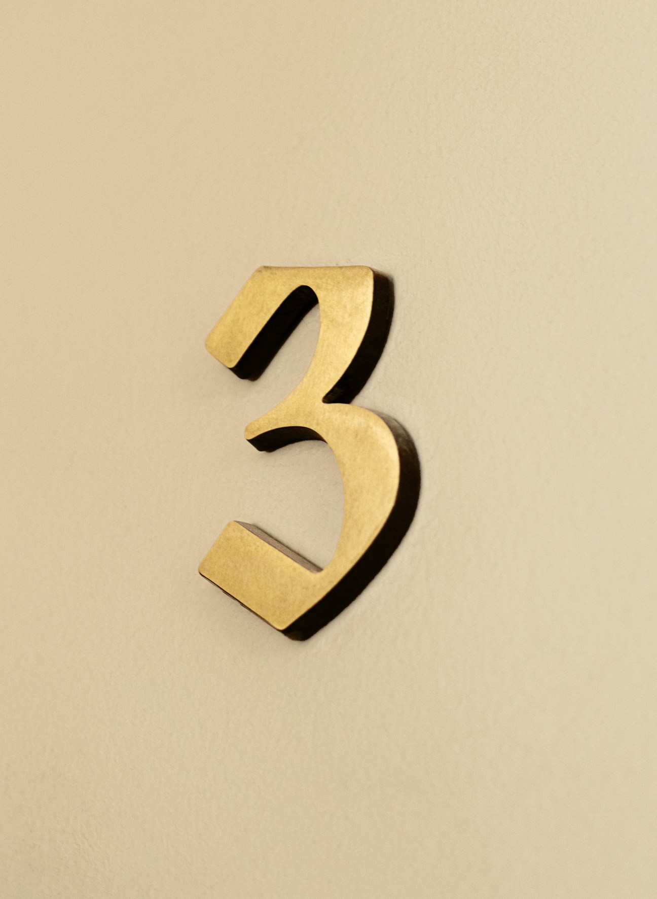 Golden number 3 mounted on beige wall