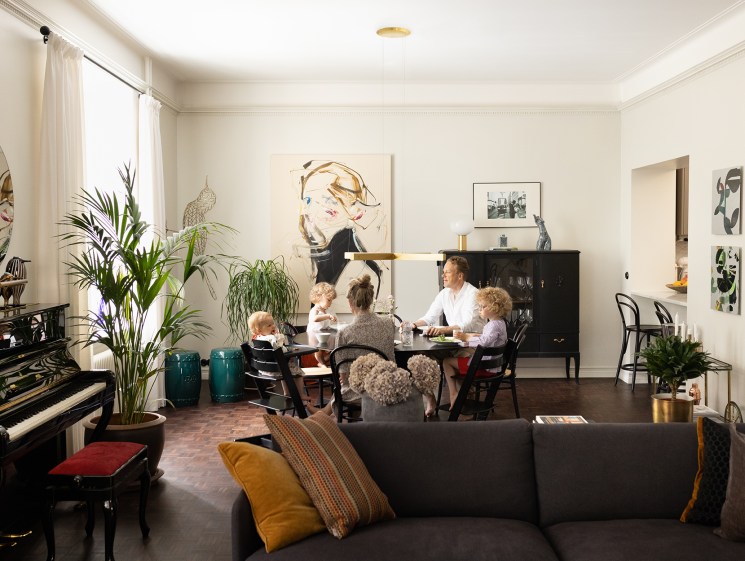 Family dining together in an eclectic living room with a piano and artwork.