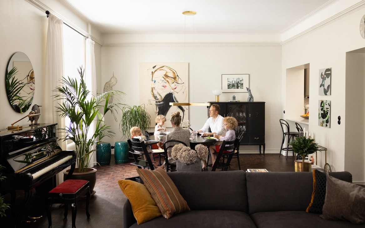 Family dining at table in modern living space with piano, plants, and contemporary art on walls
