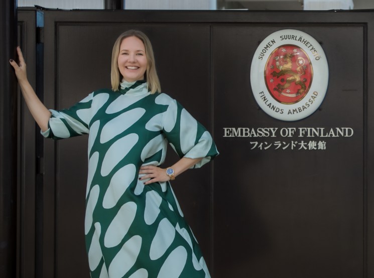 Reetta Purontakanen standing outside the Embassy of Finland in Japan wearing a green and white patterned dress