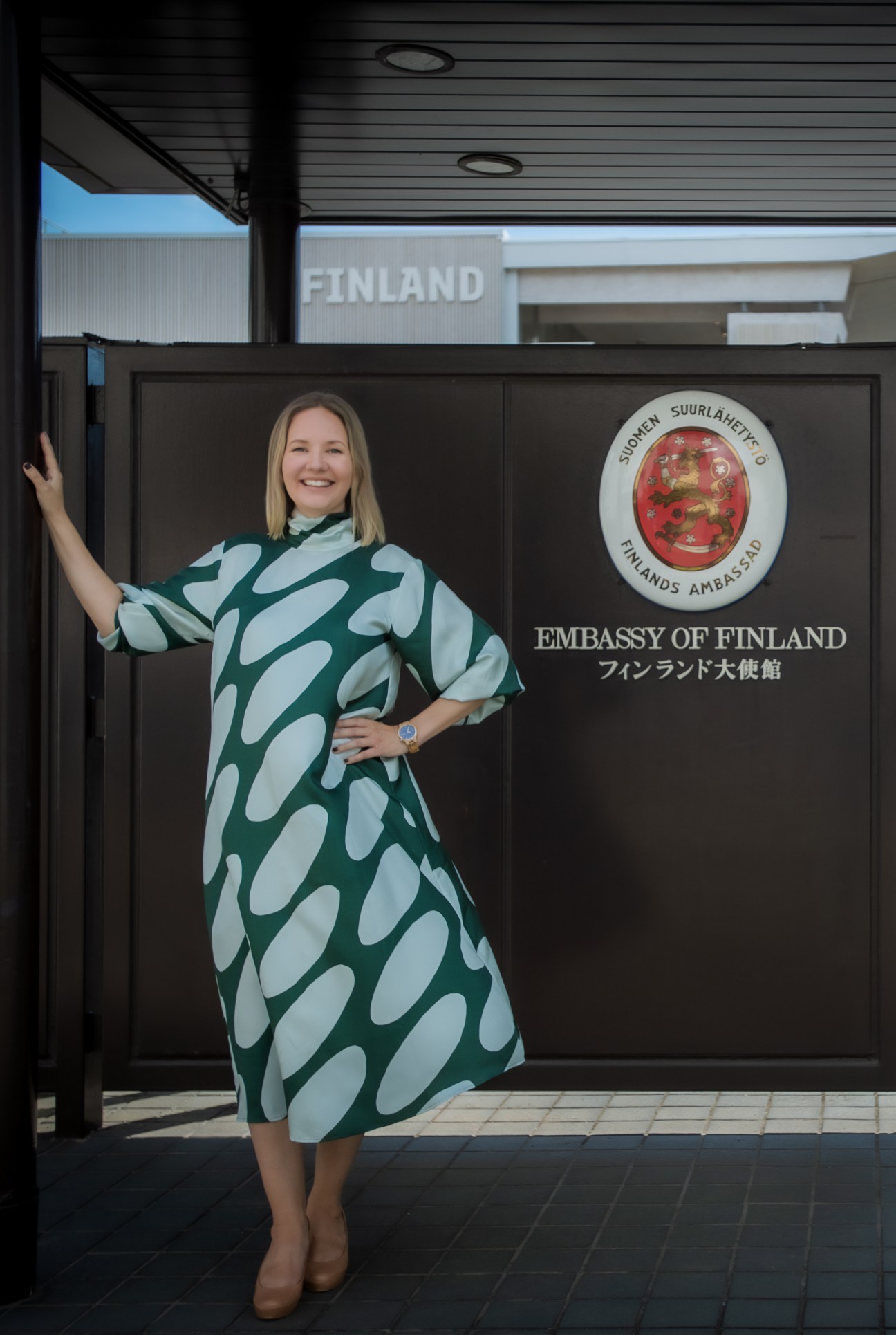 Reetta Purontakanen standing outside the Embassy of Finland in Japan wearing a green and white patterned dress
