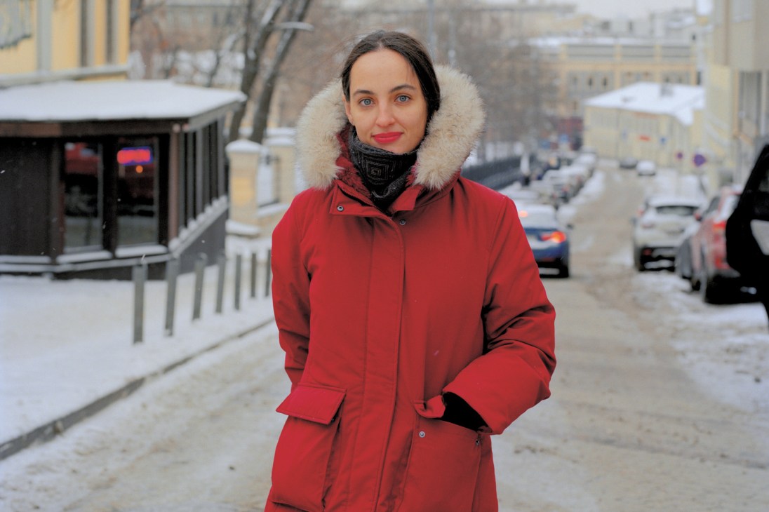 Elena Kostyuchenko in a red winter coat with fur-trimmed hood standing on a snowy street
