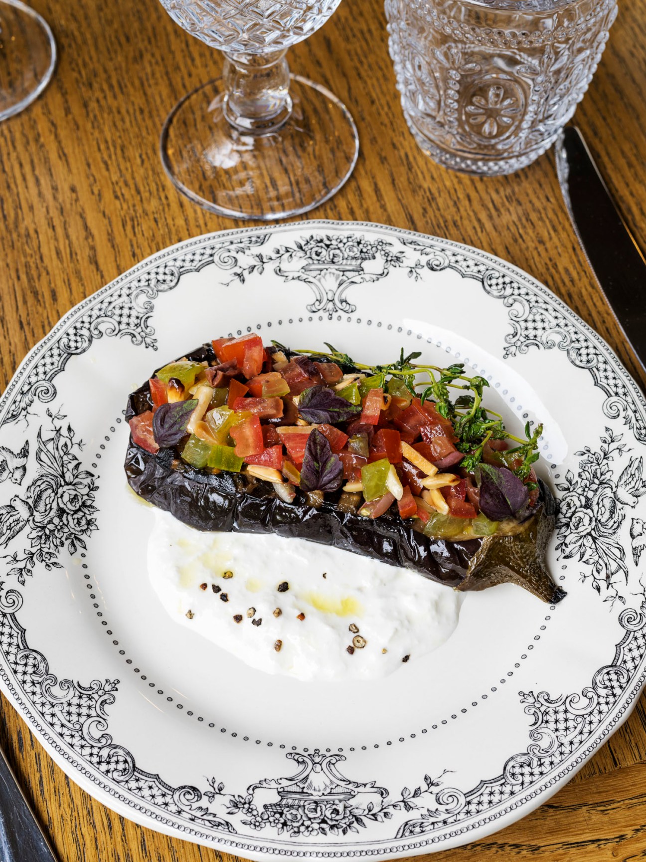 Grilled aubergine topped with diced tomatoes and burrata cheese served on decorative white plate