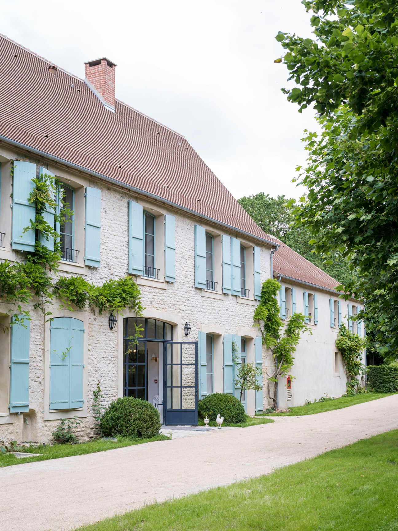 Traditional Norman stone building with pale blue shutters and terracotta tile roof surrounded by manicured gardens