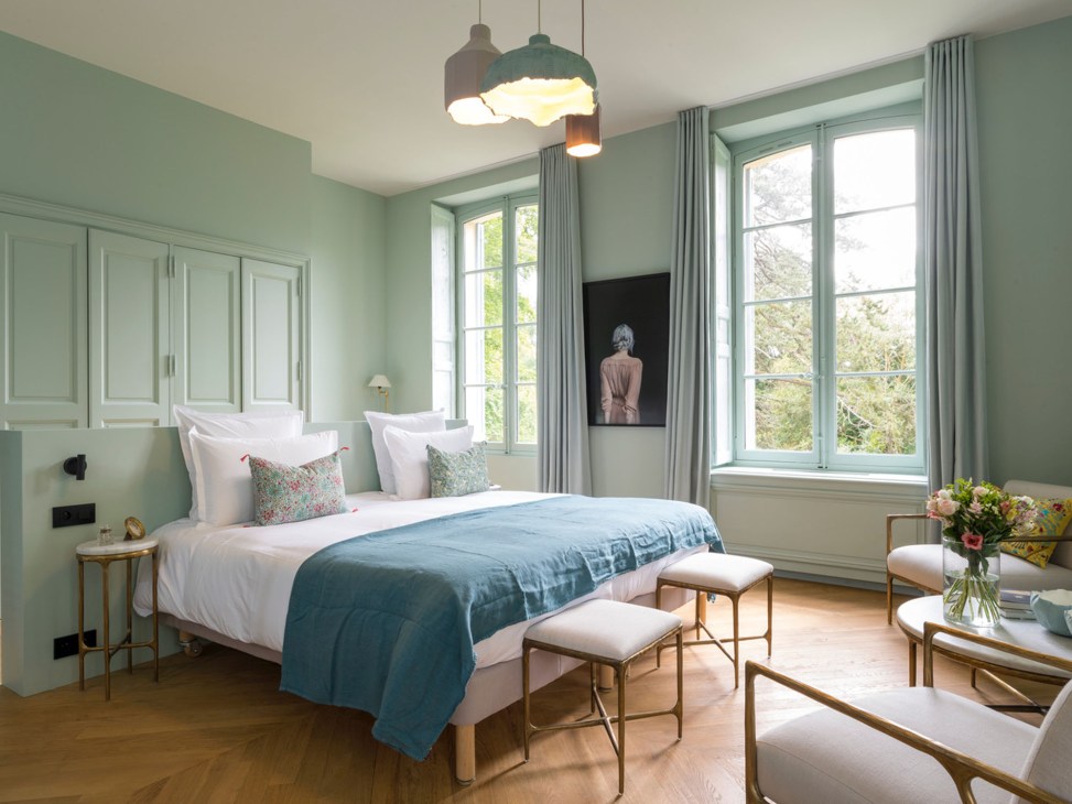Hotel suite with sage green walls, white bedding, blue throw, pendant lights and Todd Hido artwork on wall