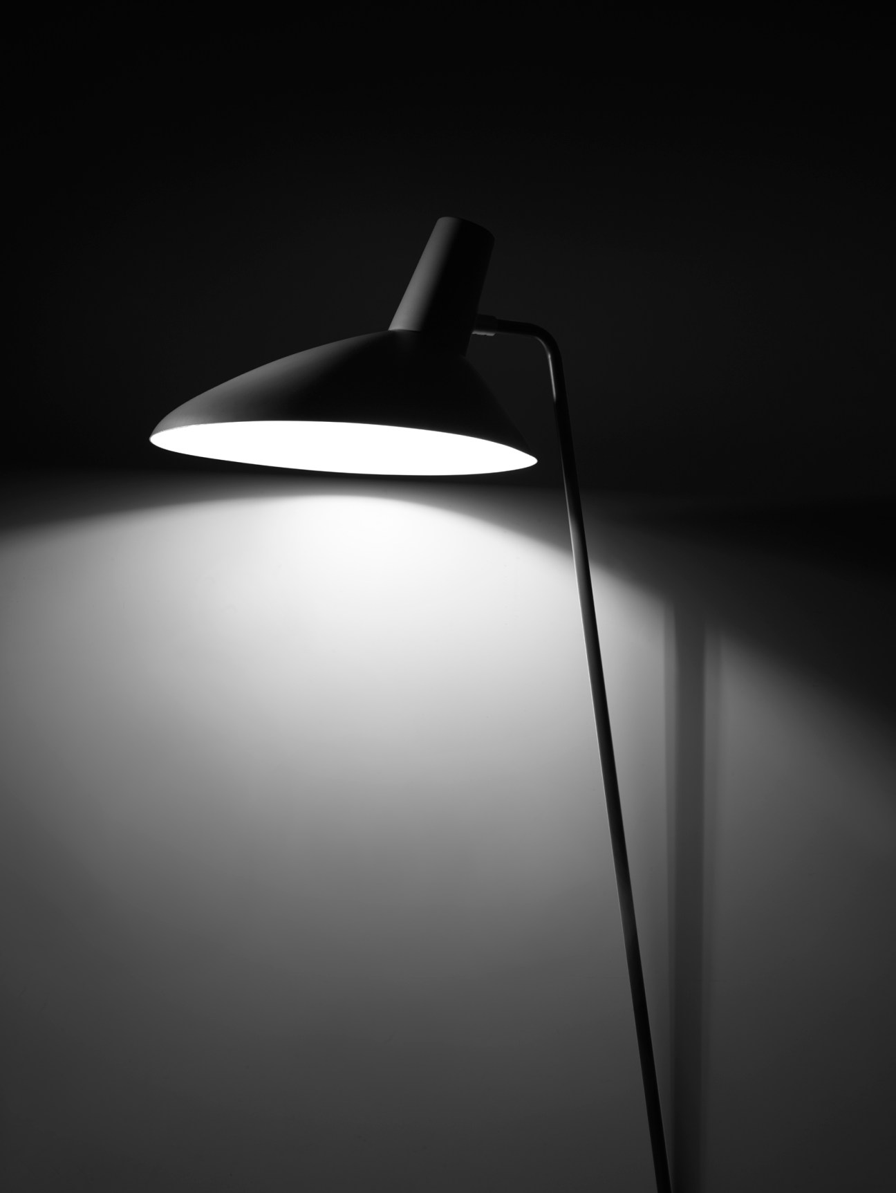 Modern black reading lamp creating focused light pool on surface against dark background