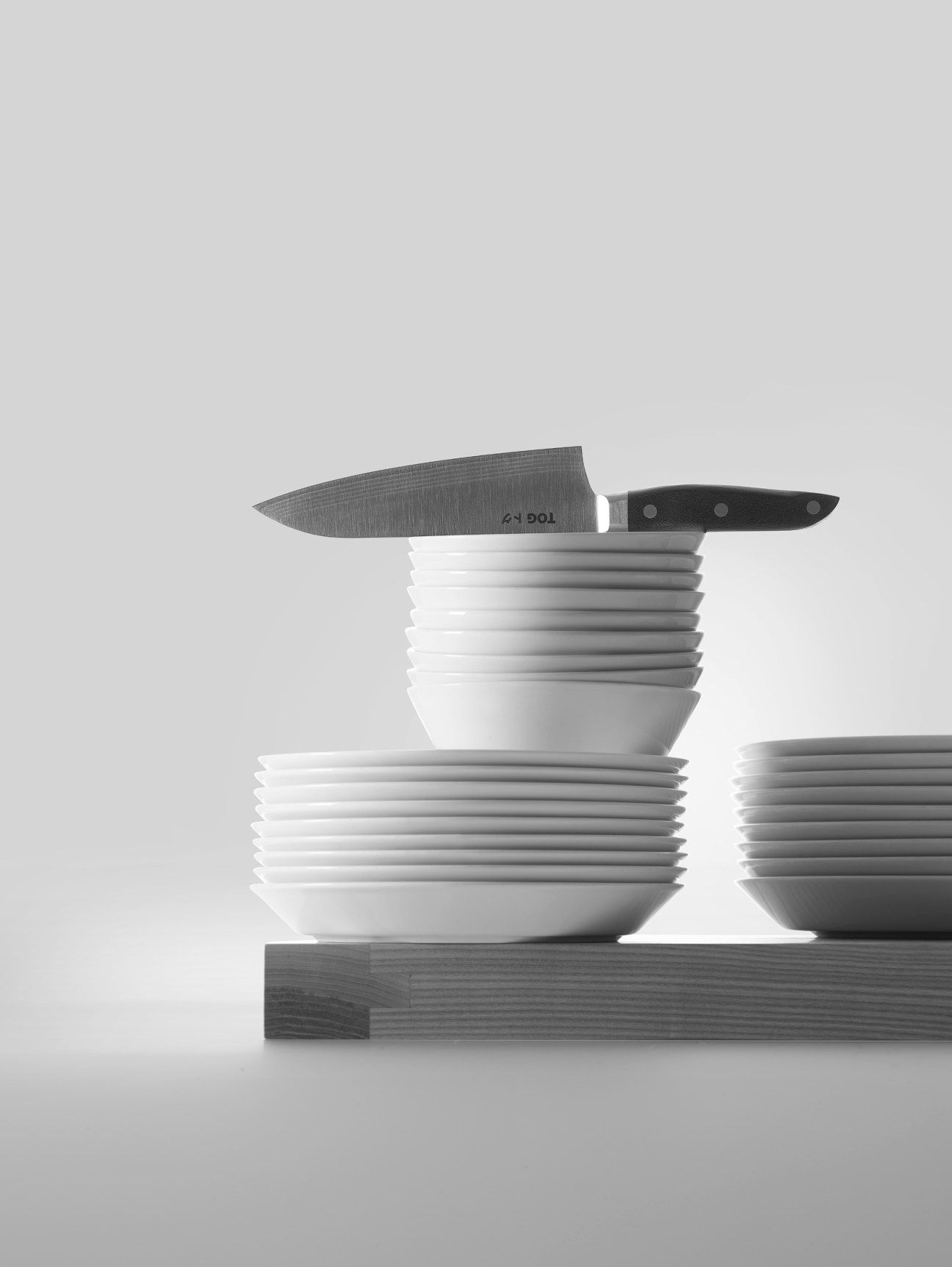 Stacks of white plates and bowls with a kitchen knife on wooden surface