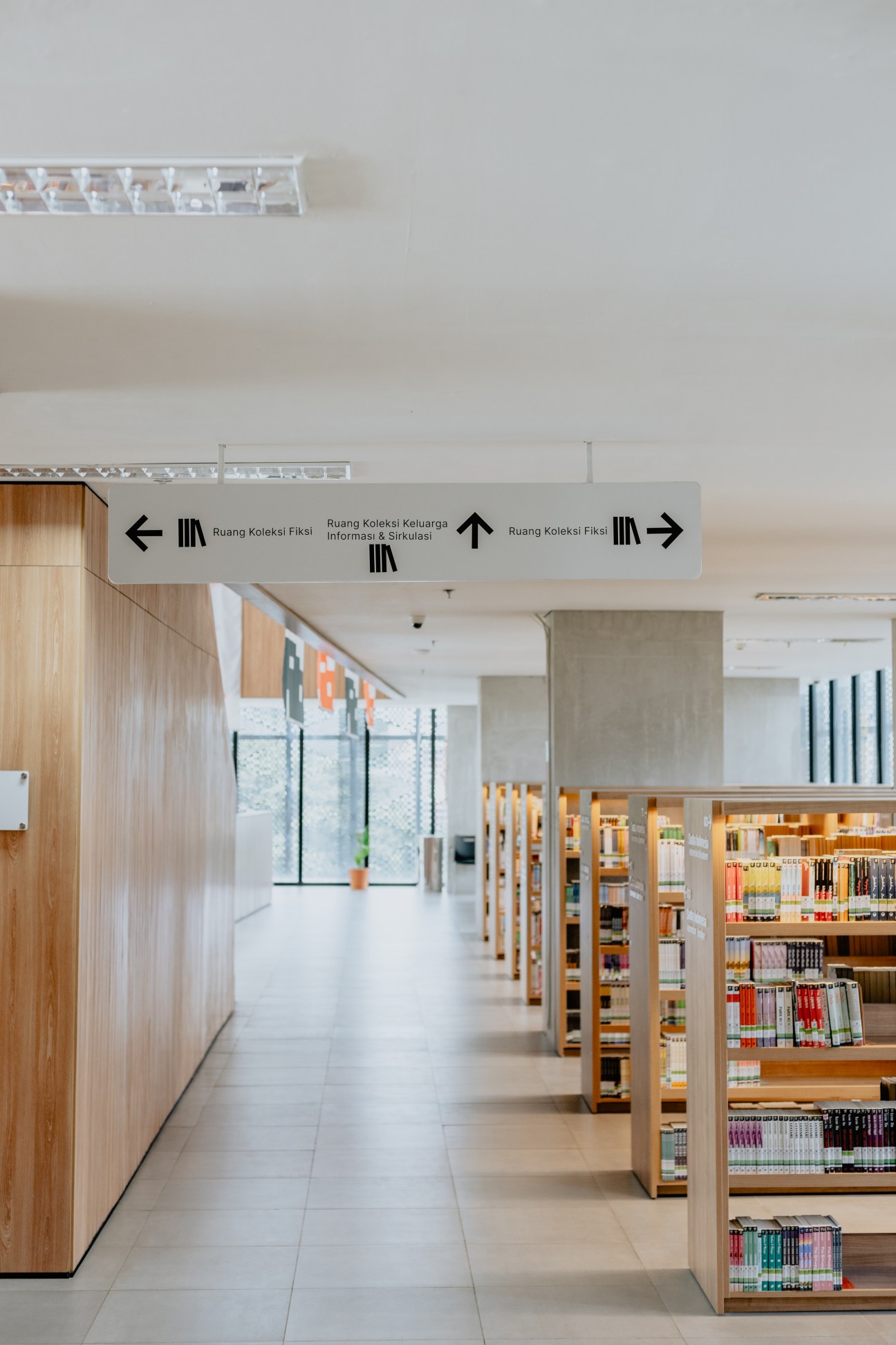 Interior of Jakarta's main public library showing wooden shelving units with books and directional signage in Indonesian.