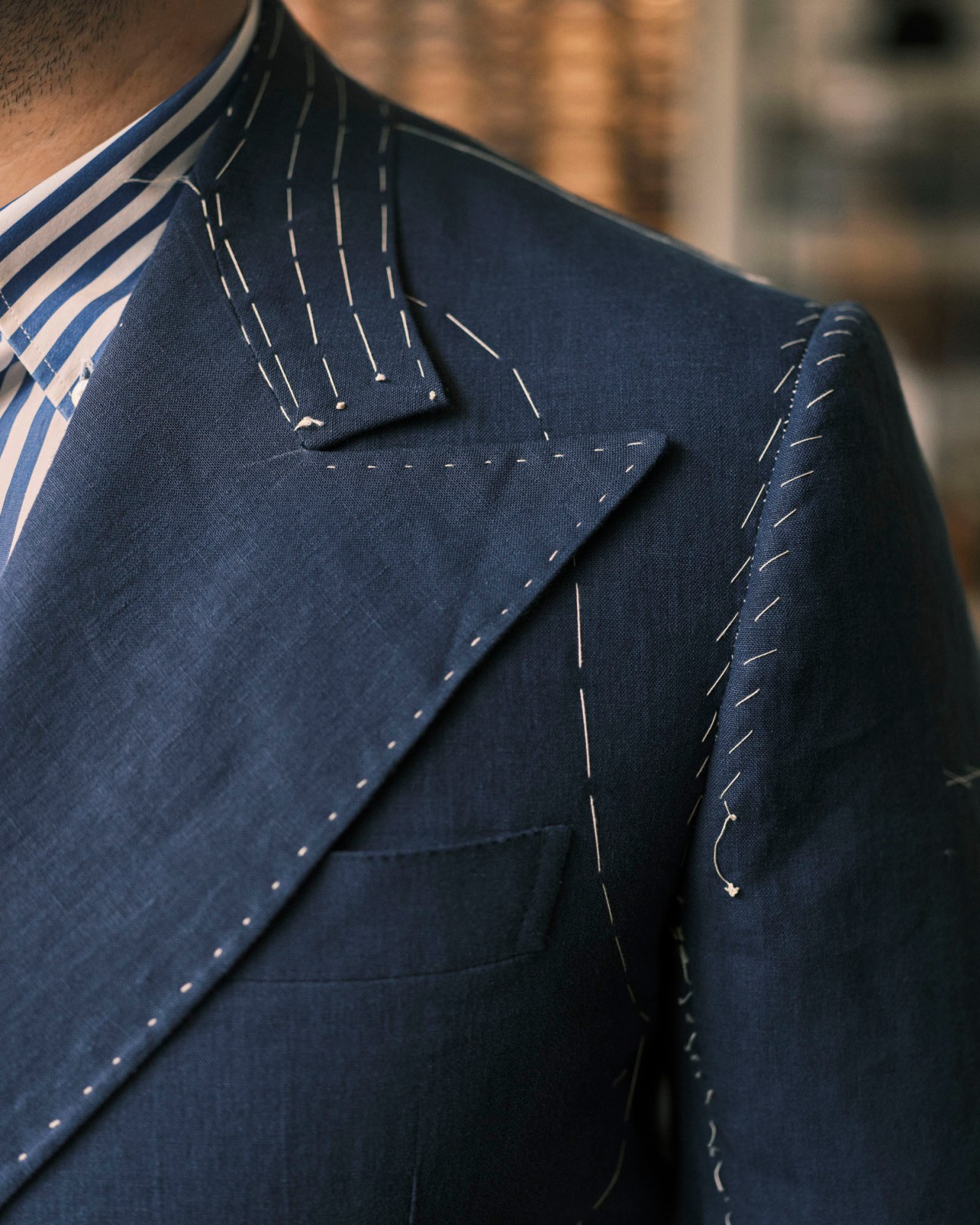 Close-up of navy suit jacket showing white basting stitches on lapel and collar during tailoring construction