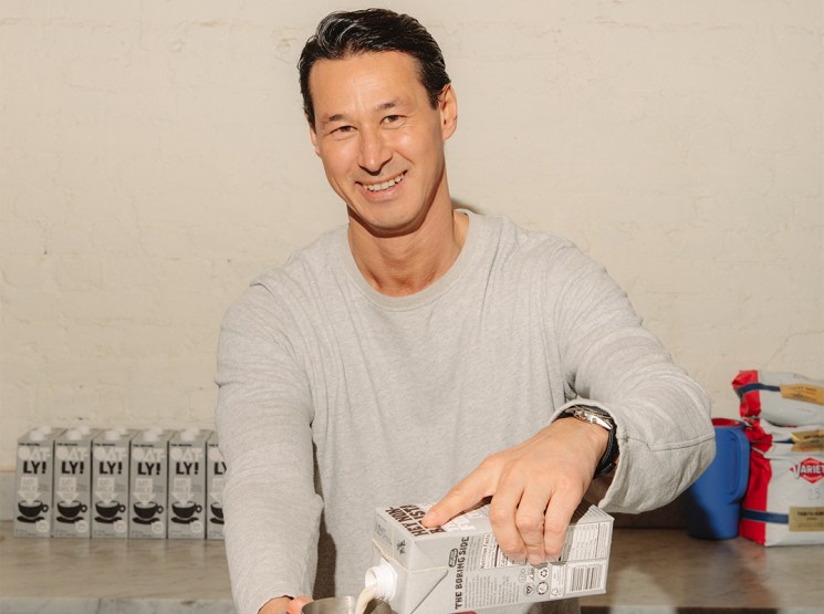 Toni Petersson, Oatly CEO, pouring oat milk into a metal pitcher at a table with Oatly cartons behind him.