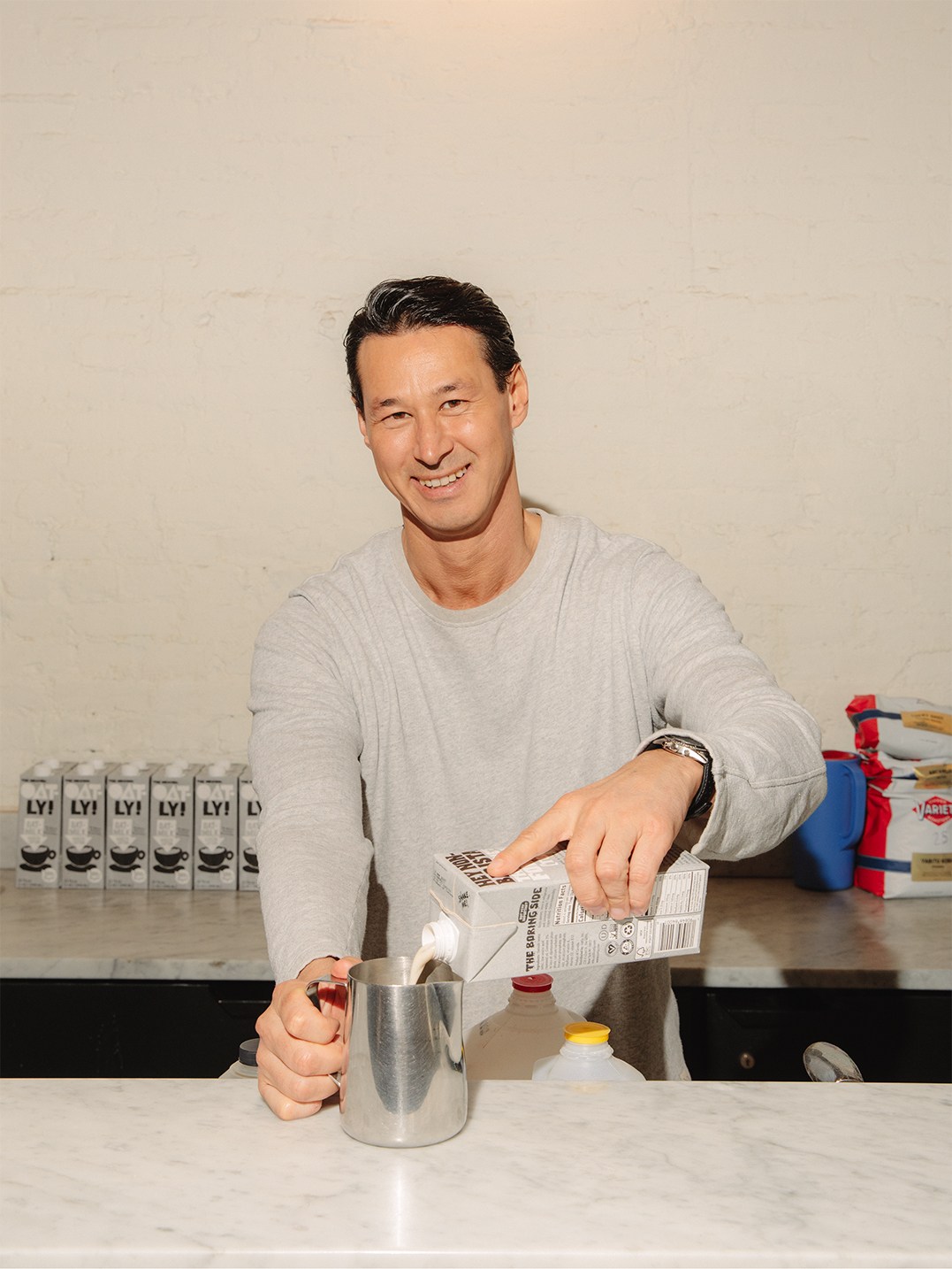 Toni Petersson, Oatly CEO, pouring oat milk into a metal pitcher at a table with Oatly cartons behind him.