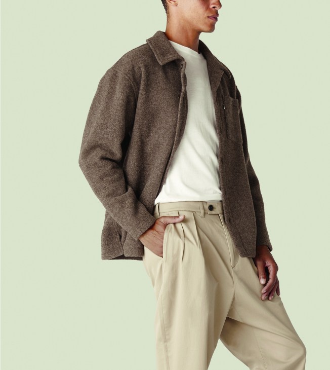 Man wearing Rier × Monocle fleece overshirt in natural brown over white t-shirt and beige trousers.