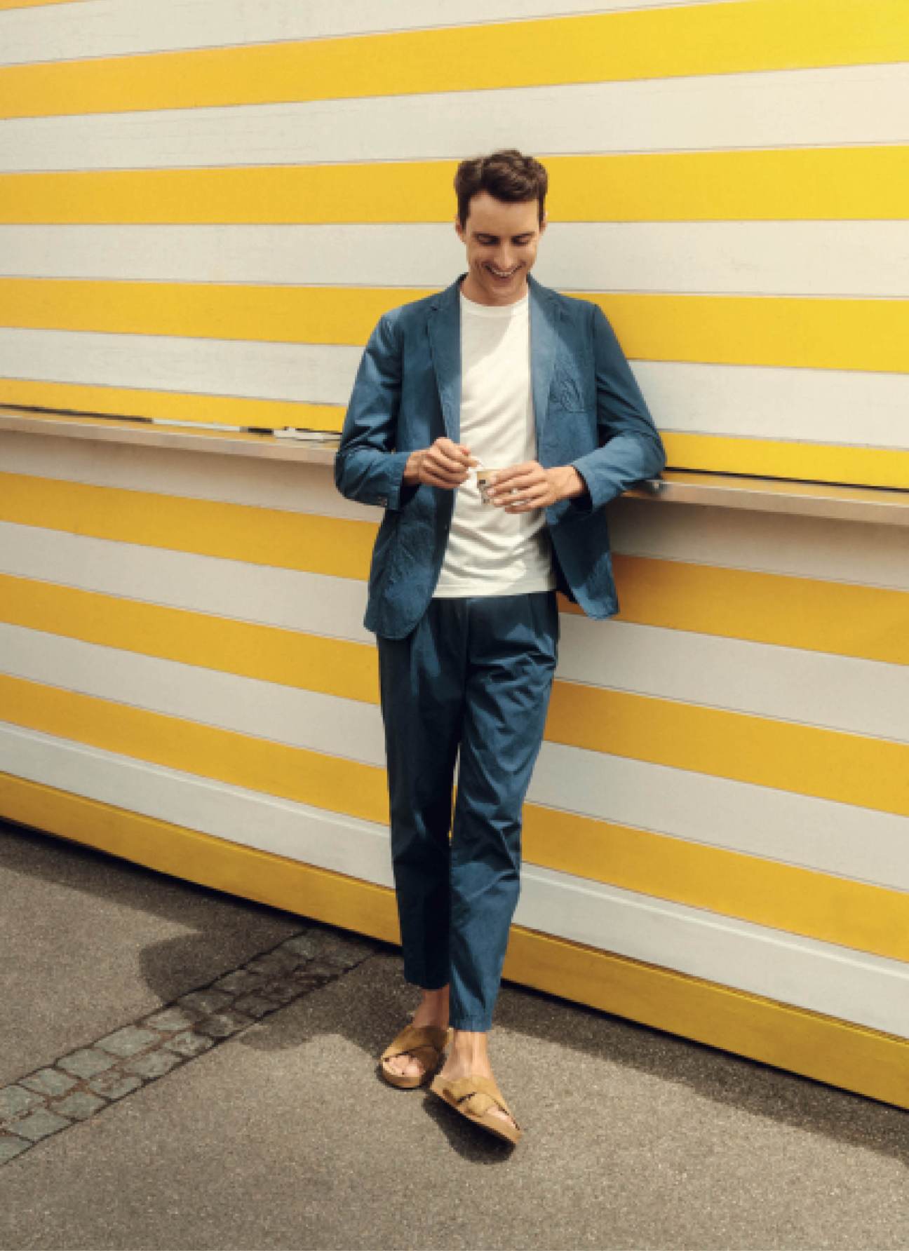 Man in blue suit by The Gigi with white t-shirt and sandals against yellow striped wall