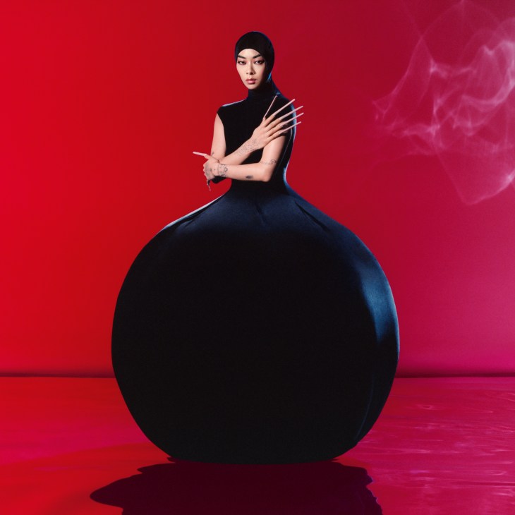 Rina Sawayama in dramatic black outfit with voluminous skirt against vibrant red background