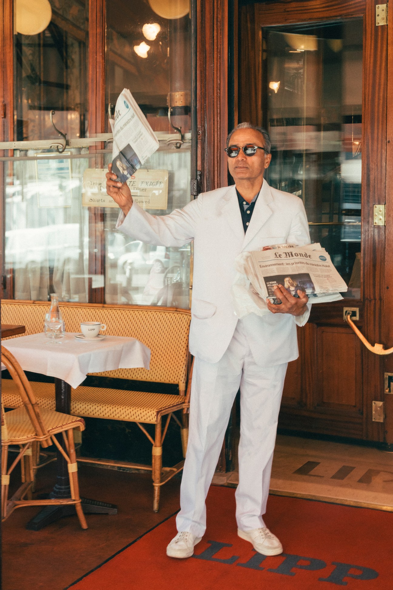 Ali Akbar, a newspaper vendor in Paris, holds Le Monde outside a café in Saint-Germain-des-Prés.