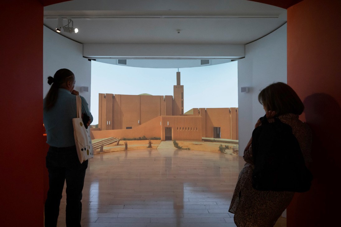 Museum visitors viewing an architectural model display in a white exhibition space