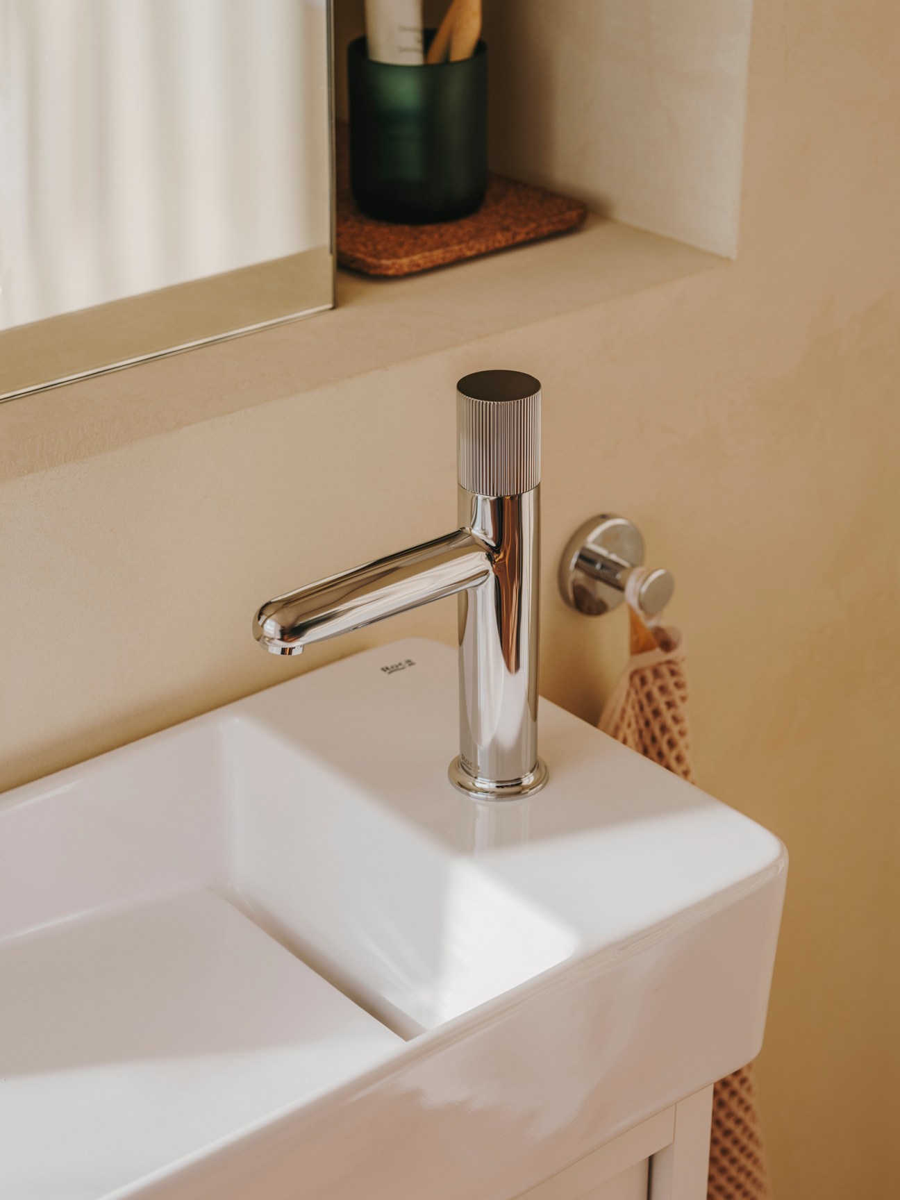 Modern chrome bathroom faucet with ridged cylindrical handle and curved spout mounted on white sink
