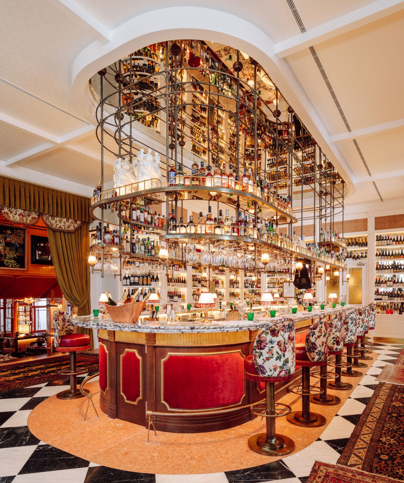 Interior of Rocco gastrobar at The Ivens hotel in Lisbon, featuring a cylindrical bar with red velvet seating, multi-tiered bottle displays, and ornate architectural details